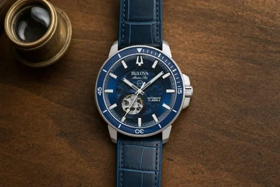 Relógio Bulova de aço sobre madeira escura ao lado de uma lupa de relojoeiro