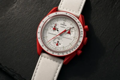 MoonSwatch de caixa vermelha fosca e pulseira branca de tecido sobre pedra escura