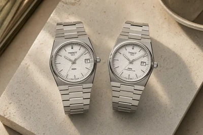 Dois Tissot PRX lado a lado sobre pedra clara, um com fundo de vidro e outro com fundo fechado